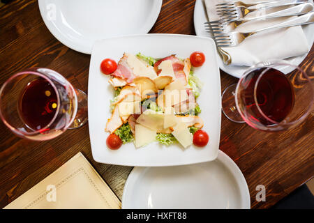 Draufsicht auf Cäsarsalat auf weißen Teller mit Gläser Rotwein serviert. Rezept oder Restaurant-Menü-Hintergrund Stockfoto