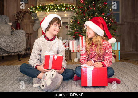 Glückliche Kinder in Santa Hut sitzt auf Teppich mit Weihnachtsgeschenke Stockfoto