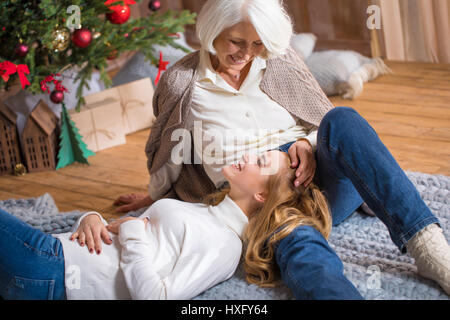 Glücklich Teenager-Mädchen auf den Knien der Großmutter dem Weihnachtsbaum liegen Stockfoto