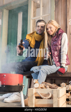 Glückliches junges Paar Bier trinken und Grill auf Veranda Stockfoto