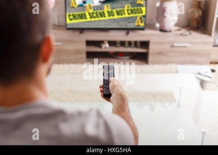 Mann mit Fernbedienung beobachtet Straftaten Serie im TV zu Hause Stockfoto