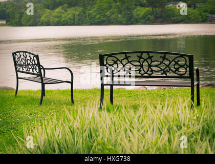 Dekorative Metall Park Bänken mit Blick auf stilles Wasser. Stockfoto