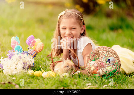Schöne lächelnde Mädchen mit niedlichen Häschen in den Korb und Ostereier auf dem Rasen im Frühling Urlaub. Blick in die Kamera. Stockfoto