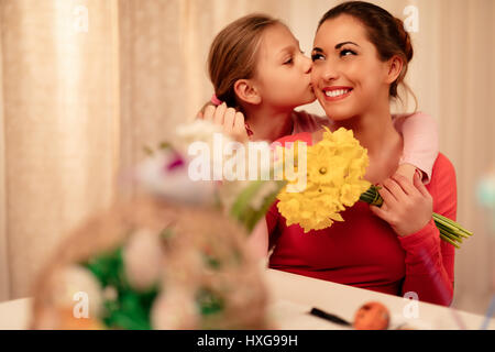 Niedliche kleine Mädchen geben ihre Mutter Blumenstrauß gelbe Narzissen und dich zu küssen. Stockfoto