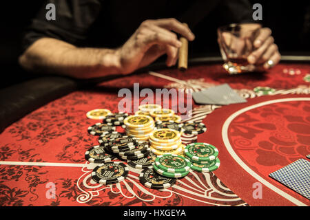 Nahaufnahme von Pokerchips am Tisch in der Nähe von Spieler mit Glas und Zigarre Stockfoto