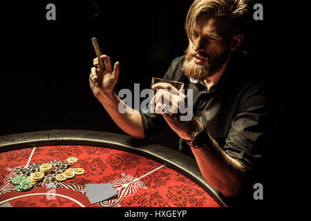 Handsome bärtiger Mann raucht Zigarre und Whisky zu trinken, beim Poker zu spielen Stockfoto