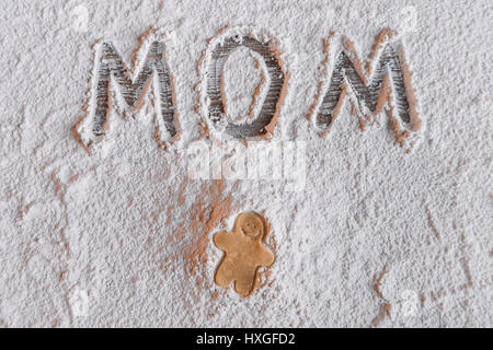 "Ansicht von rohem Lebkuchen Mann und Wort Mom in Mehl, Mütter Tag Konzept geschrieben von oben Stockfoto