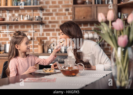 "Seitenansicht Fütterung Mutter Tochter mit Kuchen am Muttertag Urlaub in Küche Stockfoto