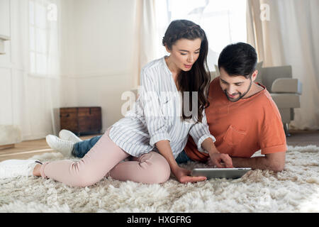 Glückliches junges Paar sitzt auf Teppich und mit digital-Tablette Stockfoto