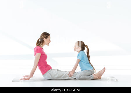 Seitenansicht der glückliche Mutter und Tochter sitzen auf Yoga-Matte und sahen einander Stockfoto