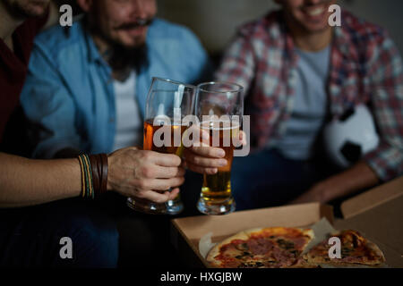 Closeup Portrait Gruppe von Freunden zu Hause treffen, sitzen auf der Couch im dunklen Raum mit Biergläsern Toasten und Pizza zu essen, während gerade footbal Stockfoto