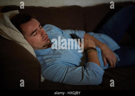 Porträt des jungen Mann Einschlafen auf Couch im dunklen Raum mit Fernbedienung beim Fernsehen spät in der Nacht Stockfoto