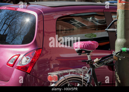 Ein Fahrrad mit einem rosa Sattel steht vor einem Auto mit der gleichen rosa Farbe. Stockfoto