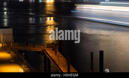 Abstrakte Langzeitbelichtung von Menschen beobachten ein Kreuzfahrtschiff verlässt den Hamburger Hafen, Deutschland in der Nacht. Stockfoto