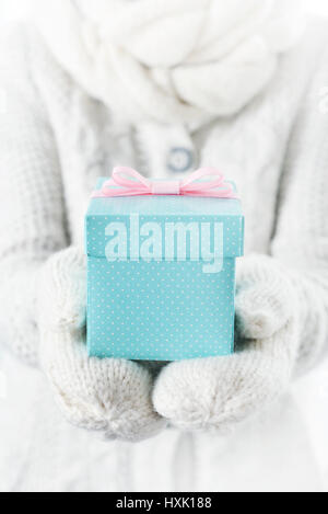 Hände im weißen Handschuhe halten kleine blaue Geschenkbox mit rosa Schleife. Stockfoto