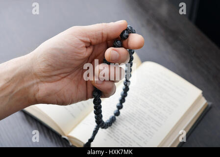 Männliche Hand mit Rosenkranz Perlen Closeup und Koran auf Hintergrund. Stockfoto