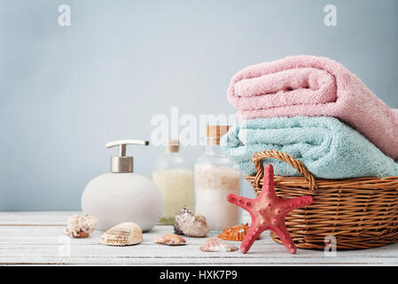 Handtücher im Korb mit Flaschen Shampoo und Meer Salz auf hellem Hintergrund Stockfoto