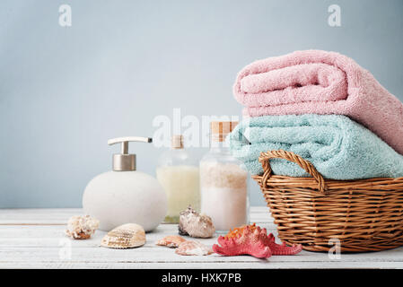 Handtücher im Korb mit Flaschen Shampoo und Meer Salz auf hellem Hintergrund Stockfoto