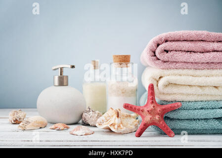 Seifenspender mit Flaschen Shampoo und Meer Salz mit Handtüchern auf hellem Hintergrund Stockfoto