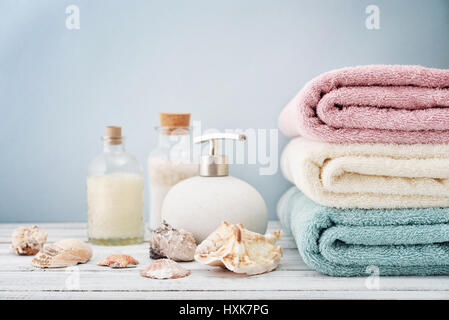 Seifenspender mit Flaschen Shampoo und Meer Salz mit Handtüchern auf hellem Hintergrund Stockfoto