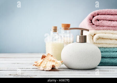 Seifenspender mit Flaschen Shampoo und Meer Salz mit Handtüchern auf hellem Hintergrund Stockfoto
