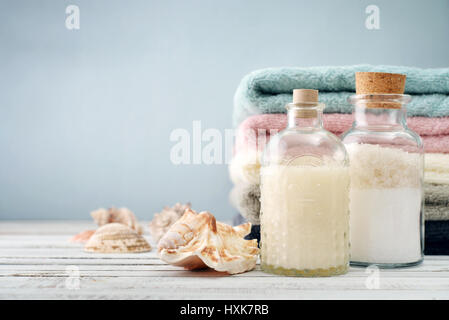 Flaschen mit Shampoo und Meer Salz mit Handtüchern auf hellem Hintergrund Stockfoto