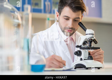 Konzentriert Man Wissenschaftler arbeiten mit Mikroskop und Notizen im Labor Stockfoto