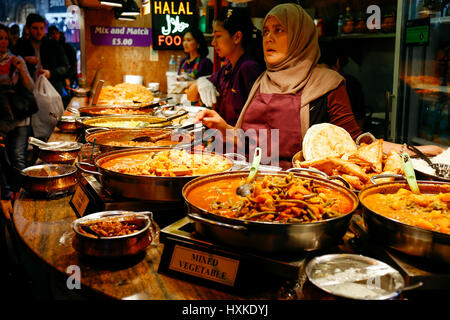 Händler auf einem Markt stall Verkauf Curry und Sorten von gekochten Lebensmitteln am Camden Market. Stockfoto