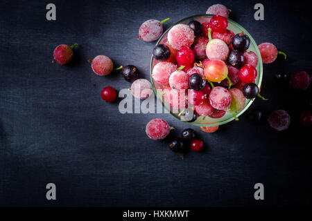 Gefrorene und frische Beeren in einem Glas pial auf einem schwarzen Hintergrund. Es ist mit Eiskristallen bedeckt. Stockfoto