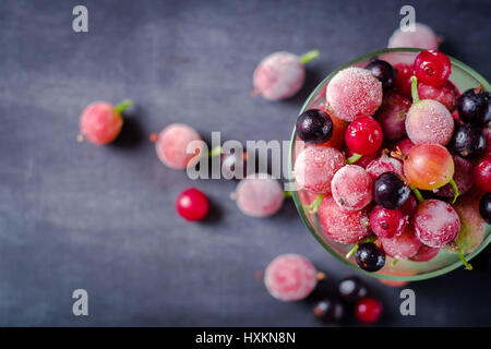 Gefrorene und frische Beeren in einem Glas pial auf einem schwarzen Hintergrund. Es ist mit Eiskristallen bedeckt. Stockfoto