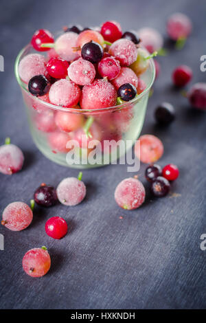 Gefrorene und frische Beeren in einem Glas pial auf einem schwarzen Hintergrund. Es ist mit Eiskristallen bedeckt. Stockfoto