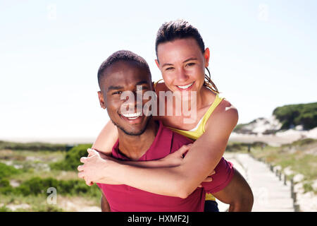 Porträt von fröhlichen jungen Ehepaar Sommer, Mann Huckepack seine Freundin im Freien genießen hautnah. Stockfoto