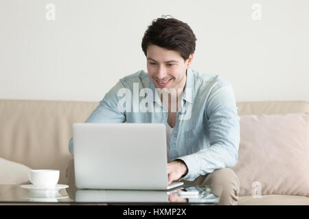 Junger Mann lächelnd, chatten, online arbeiten mit Laptop-computer Stockfoto