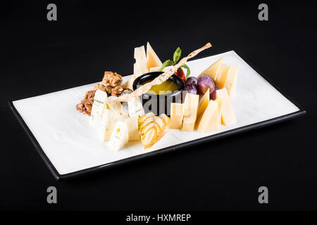 Einen großen Teller mit einer großen Auswahl an Snacks wie Käse, Walnüsse, Trauben, Cracker auf dunklem Hintergrund. Stockfoto