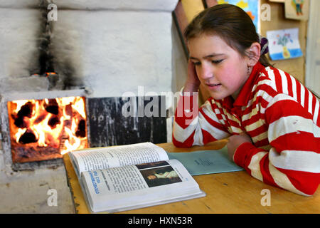 Twer, Russland - 2. Mai 2006: Russische Schülerin liest Lehrbuch sitzen neben einem offenen Kamin Holzofen. Stockfoto