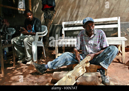 Namanga, Tansania - 9. Februar 2008: Afrikanische schwarze Holz-Carver, Kunstwerkstatt arbeiten. Dunkelhäutige Afrikaner, master Holzschnitzerei, Schnitzerei woode Stockfoto