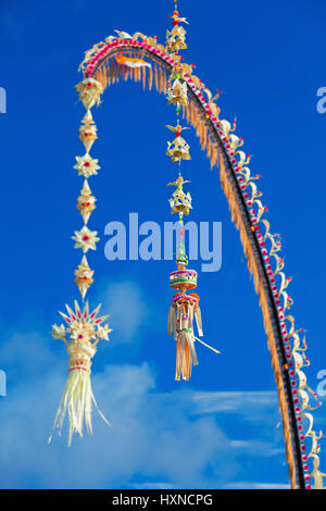 Traditionelle Bali Penjor Bambusstange mit Dekoration auf Dorfstraße vor Balinesen Häuser und Tempel auf Galungan, Kuningan Urlaub Stockfoto