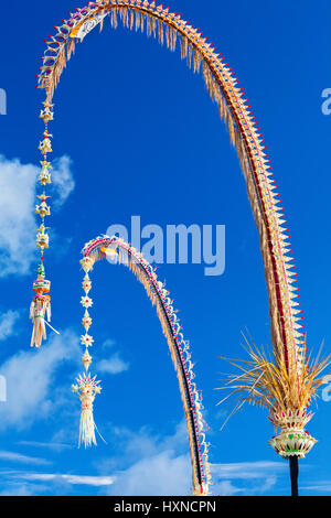 Traditionelle Bali Penjor Bambusstange mit Dekoration auf Dorfstraße vor Balinesen Häuser und Tempel auf Galungan, Kuningan Urlaub Stockfoto