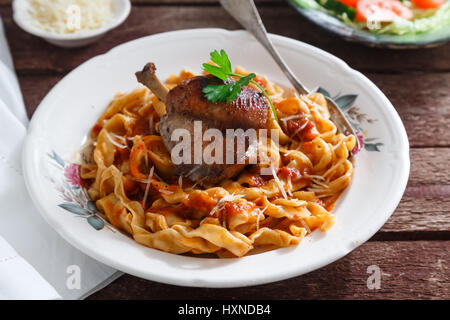 Geschmorte Kaninchenkeule in Tomatensauce mit hausgemachter Pasta, rustikal dunkel Stockfoto