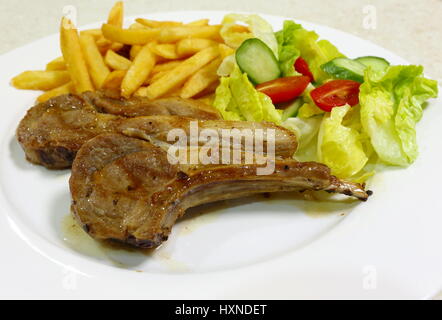 Zwei Gegrillte Lammkoteletts serviert mit französischer gebratene Kartoffelchips und Salat aus Kopfsalat, Tomaten und Gurken. Stockfoto