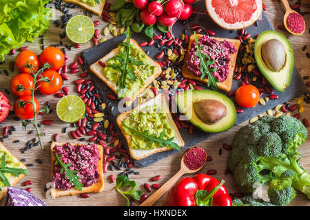 Gesunde vegane Ernährung. Sandwiches und frisches Gemüse auf hölzernen Hintergrund. Detox-Diät. Verschiedene bunte frische Säfte. Ansicht von oben Stockfoto