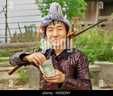 GUIZHOU PROVINZ; CHINA - APRIL 10: Mann Miao ethnische Gruppe, mit einer Muskete auf seiner Schulter verdient zählt Yuan im Dorf Festival 10. April 2010. BAS Stockfoto