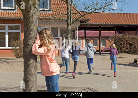 Kinder in der Grundschule spielen verstecken und suchen in Pause Stockfoto