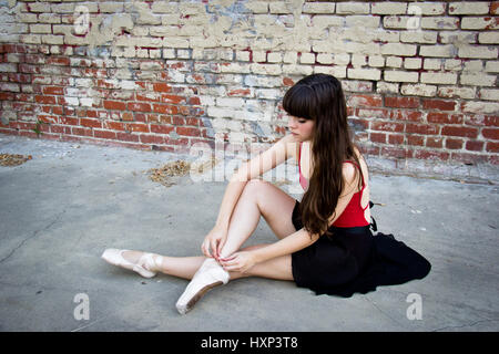 Junge Brünette Ballerina sitzen in einer Gasse, die ihre Punkt-Schuhe anziehen. Stockfoto