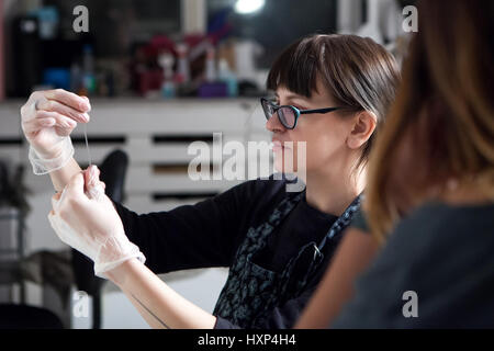 Junge süße Mädchen Tattoo Meister bei der Arbeit auf Musterung auf dem Modell Körper. Konzentration und Fokussierung auf wichtige Angelegenheit Stockfoto