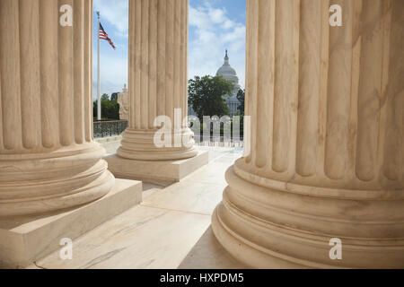 Nahaufnahme der Spalten des Supreme Court Gebäude mit einer amerikanischen Flagge und dem US Capitol im Hintergrund Stockfoto