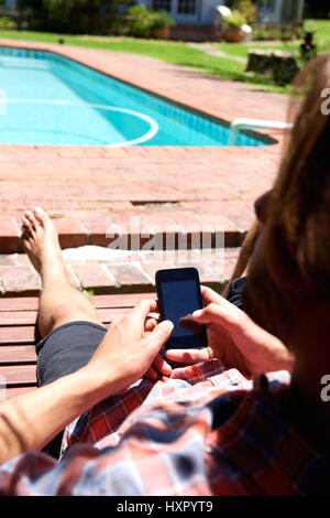 Porträt von hinten junger Mann mit Smartphone Pool Stockfoto