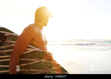 Porträt von Surfer am Strand mit Blick auf Wellen während des Sonnenuntergangs Stockfoto