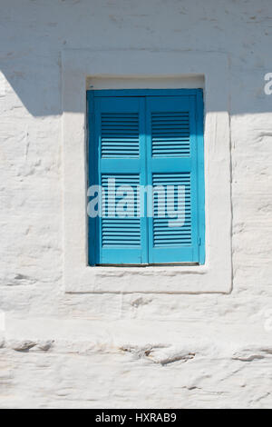 Helle blaue Fensterläden in weiß getünchten Wand, geschlossen am Mittag auf der Insel Schinoussa, Kykladen, Griechenland Stockfoto