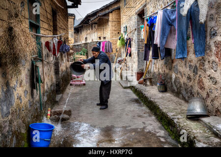 Yangshuo, Guangxi, China - 29. März 2010: Alter Bauer gießt Wasser aus einem Eimer auf einer schmalen Straße in ein Bauerndorf, in der Nähe von Seil hing, trockenen cl Stockfoto